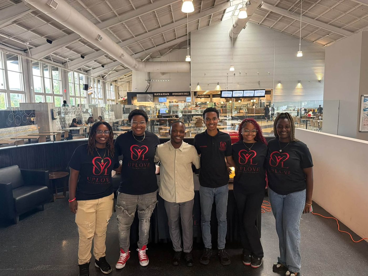 UpLove Foundation team members in matching black foundation shirts posing together in the Alabama State University cafeteria