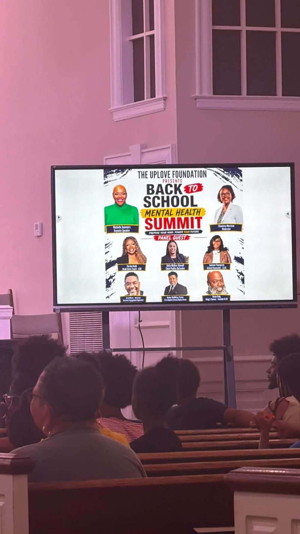 Summit attendees seated in pews watching the presentation slide introducing the keynote speaker and panel guests