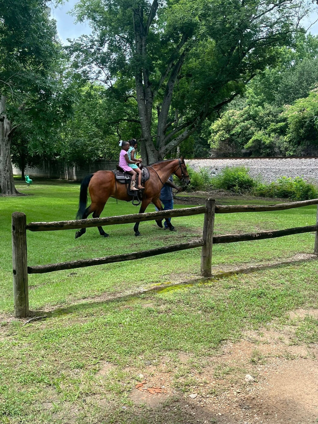 Two girls riding a horse guided by an adult on a grassy lawn