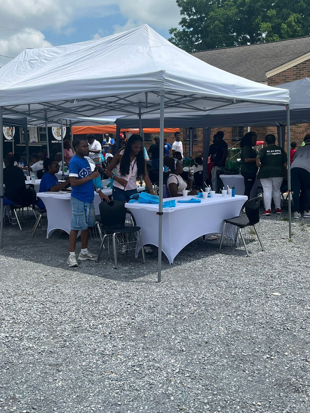 Attendees and volunteers mingling under white event tents on a gravel lot