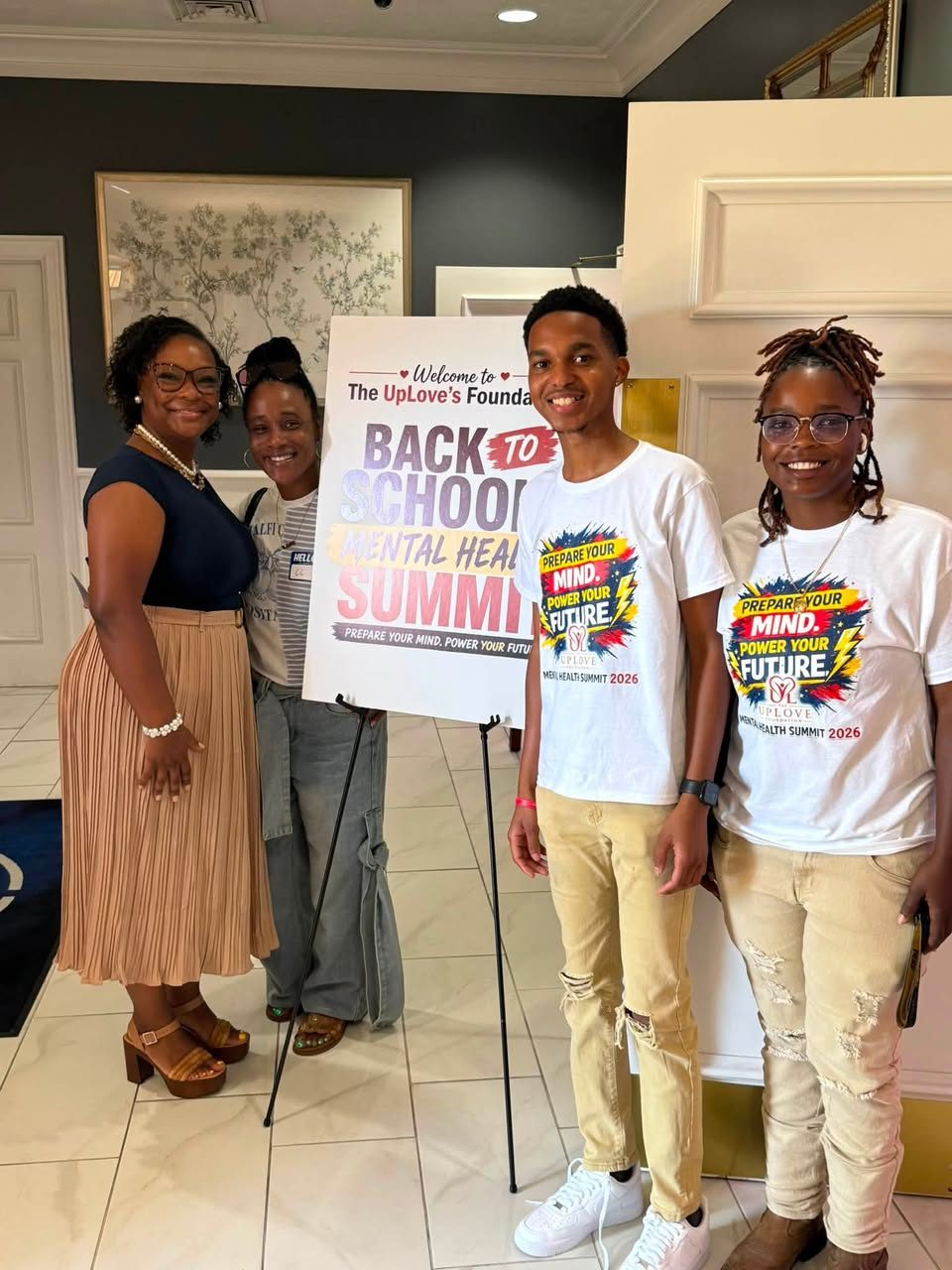 Team members and a guest posing beside the welcome sign for the Back to School Mental Health Summit