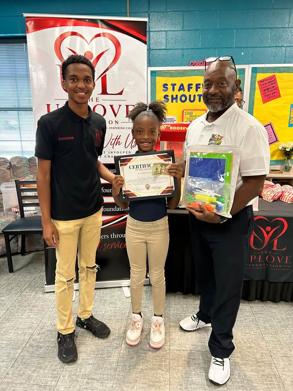 A Fitzpatrick Elementary student holding her recognition certificate beside Isaiah and a school staff member