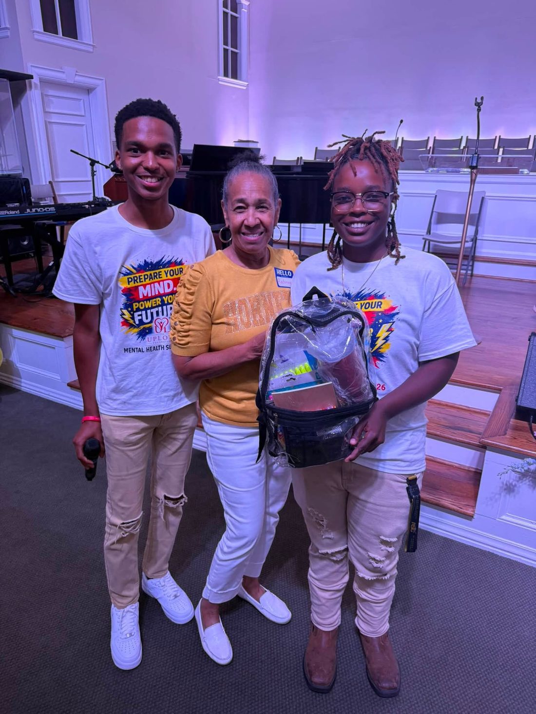 Volunteers presenting a clear backpack filled with school supplies to a guest on stage