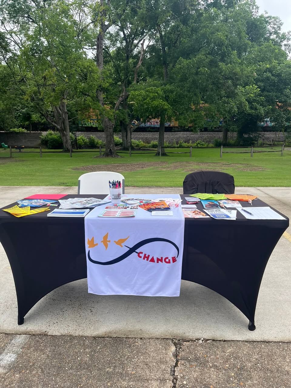 C.H.A.N.G.E. information table with a white banner runner, flyers and pens set out in front of a grassy lawn