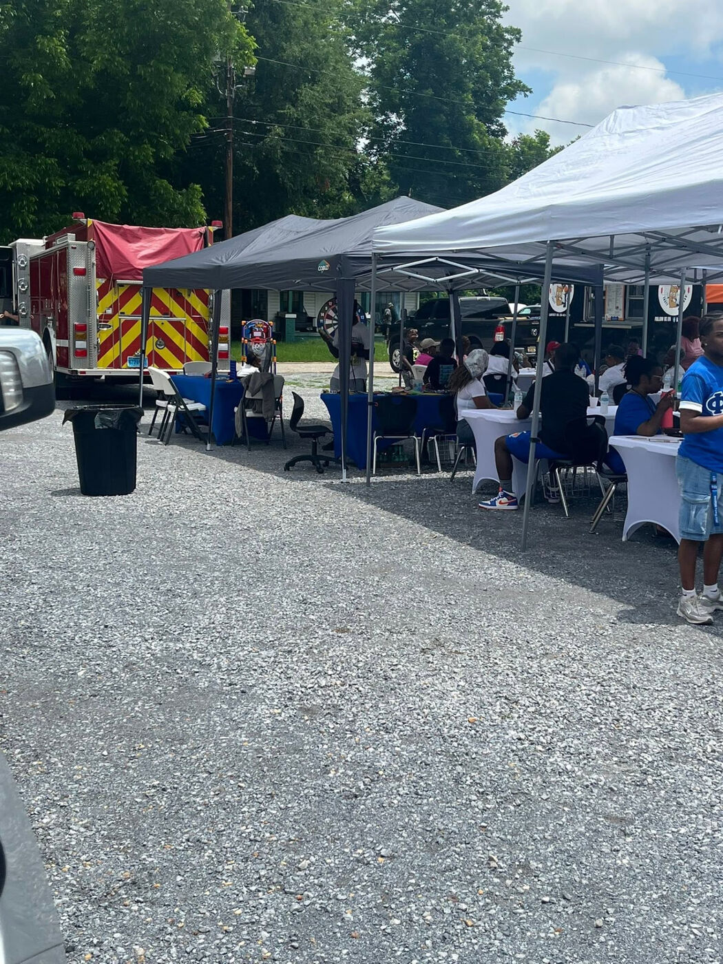 Community event with pop-up canopies sheltering tables and a fire truck parked nearby